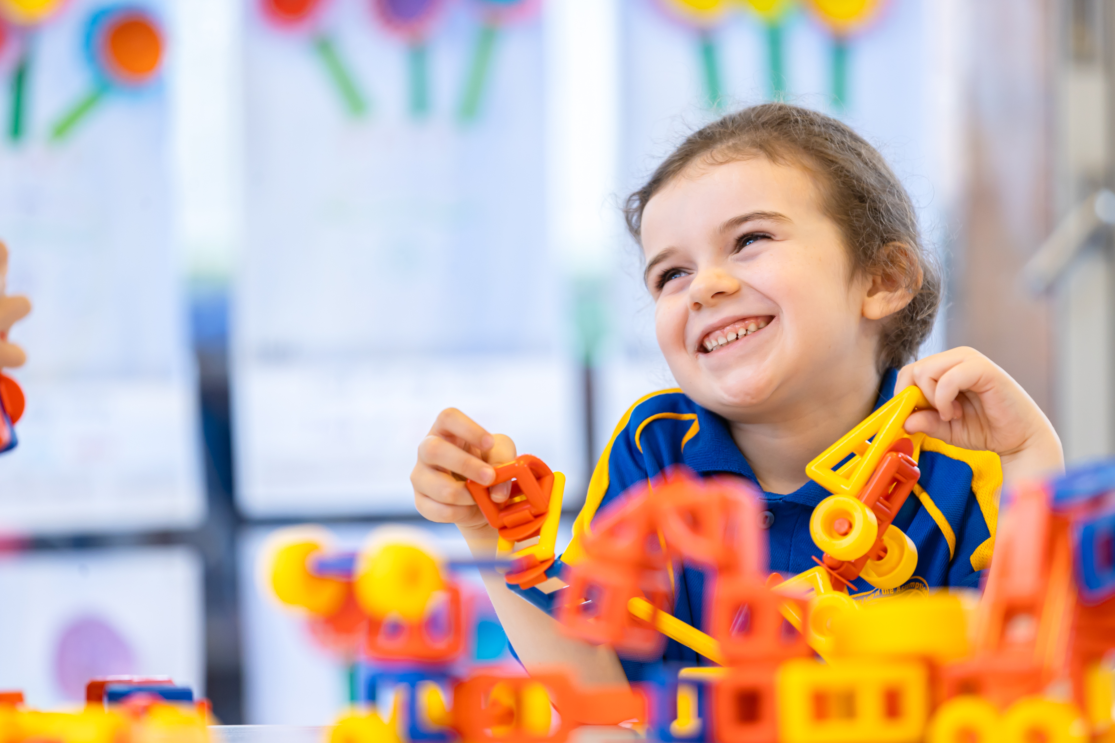 Young student smiling while playing with colourful construction blocks at a table